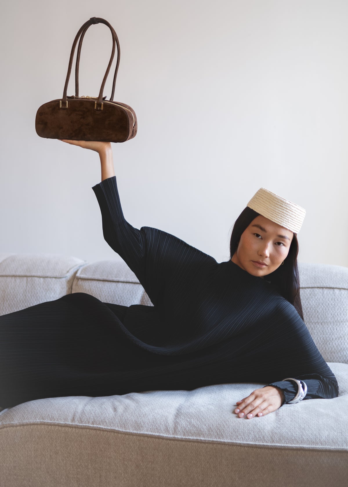 chica japonesa acostada sobre sofá con bolso café de gamuza en la mano