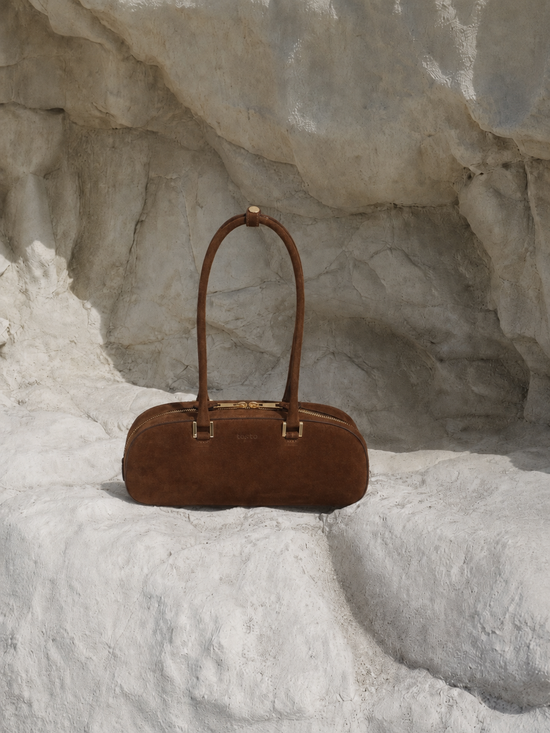 cartera café de gamuza sobre piedra blanca